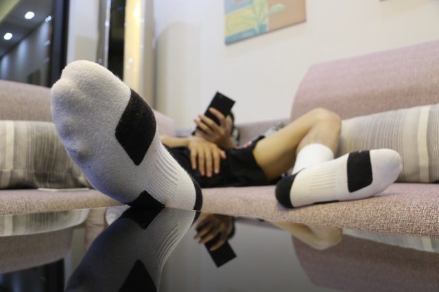 A person wearing athletic socks relaxes on a couch while looking at their phone.