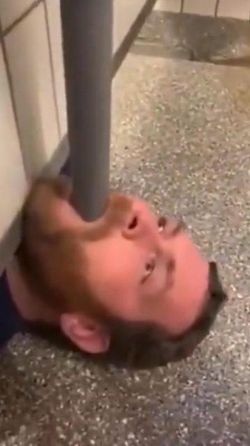 A man with a beard and ear piercing lies on a tiled floor with a pipe in his mouth.