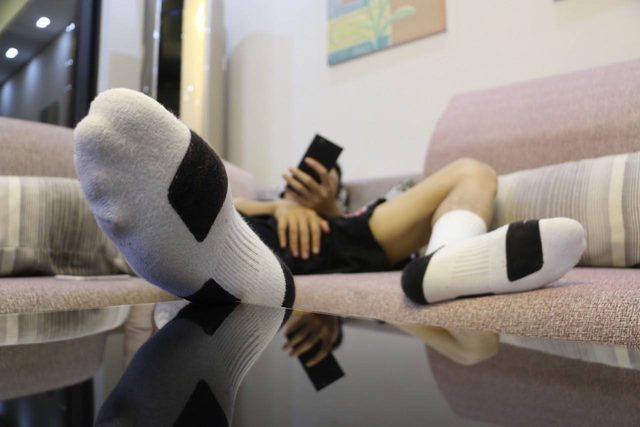 A man wearing white and black socks relaxes on a couch while looking at his smartphone.