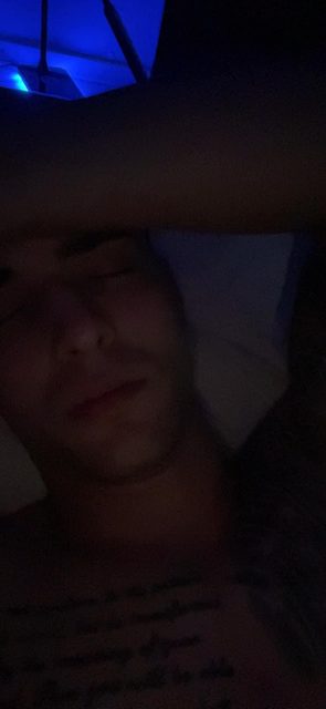 A man with tattoos is sleeping in a dark room.