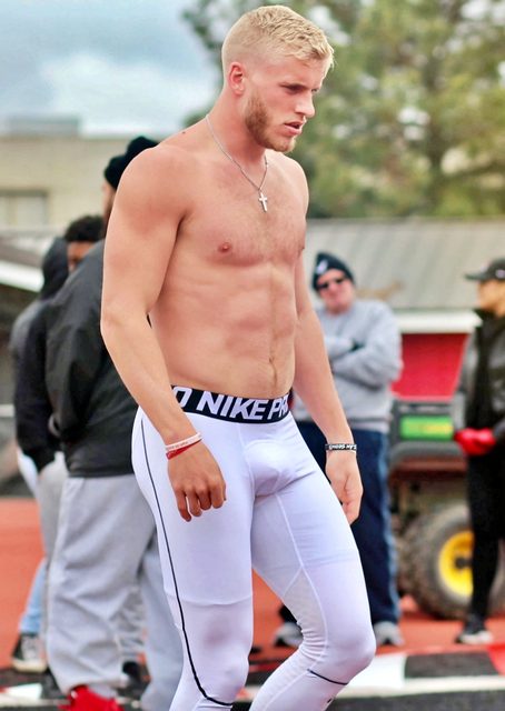 A shirtless blond jock with a muscular build wears white Nike compression leggings in an outdoor athletic setting.