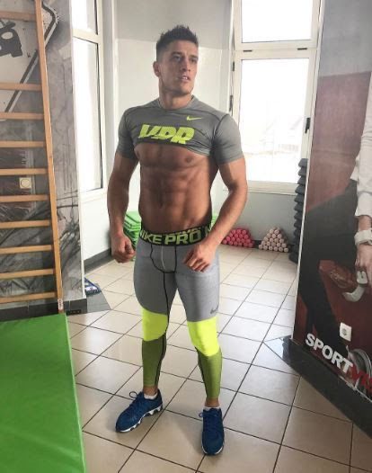 A muscular man poses in sportswear in a gym.