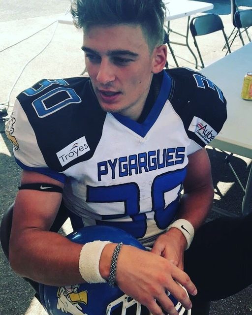 A young man in an American football uniform sits outdoors with his helmet in his lap.
