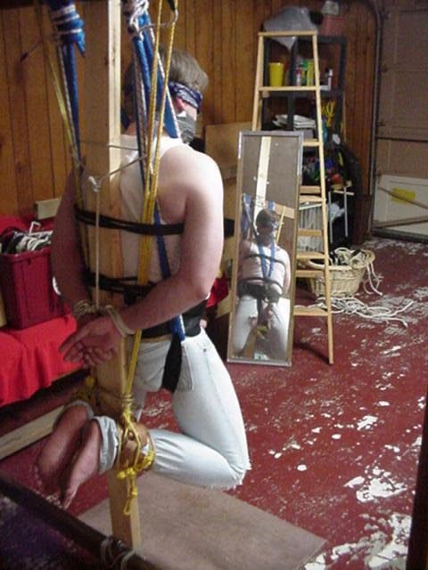 A person is blindfolded and suspended by ropes and a wooden frame indoors.