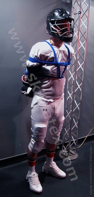 A man in a sports uniform and helmet is tied with blue rope.