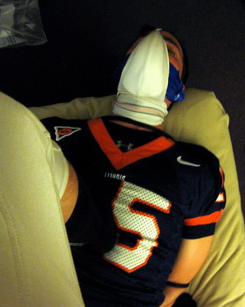 A person wearing a sports jersey is blindfolded and restrained on a bed.