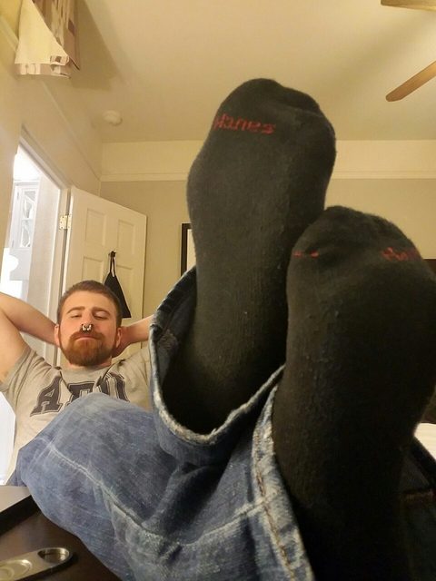 A man wearing jeans and black socks relaxes with his feet up.