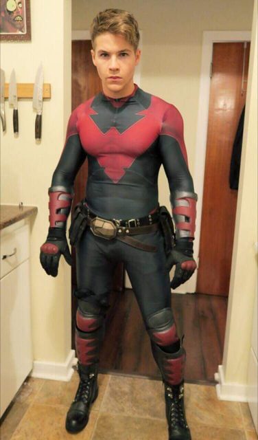 A young man in a red and black full body uniform suit poses indoors.