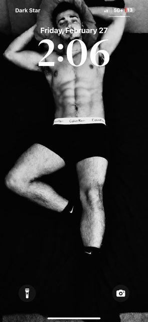 A muscular man lies on a bed wearing underwear and socks.