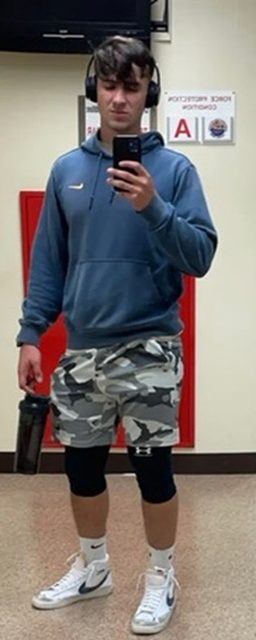A young man in sportswear takes a mirror selfie in a gym.