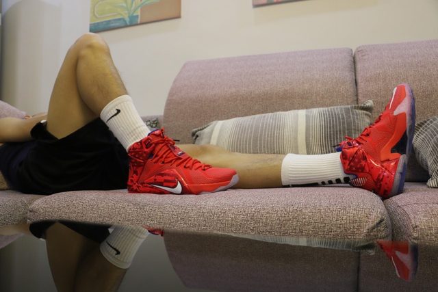 A person in red athletic sneakers and white socks lounges on a sofa.