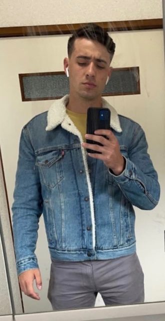 A young man in a denim jacket with a sherpa lining takes a mirror selfie.