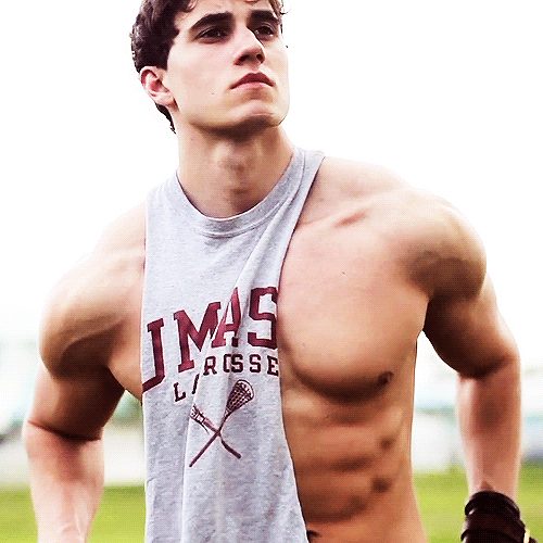 A muscular man in a grey lacrosse tank top stands outdoors.