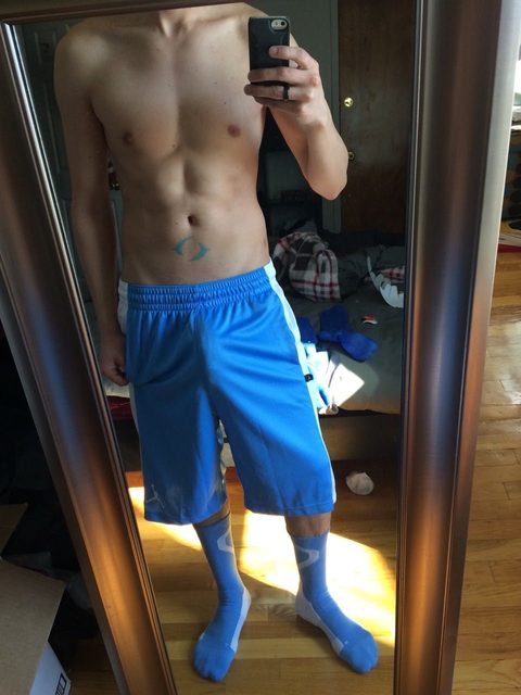 A shirtless person in blue shorts and socks takes a mirror selfie.