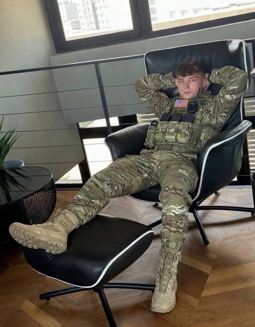 A young man in military uniform and boots relaxes in a chair with his feet up.