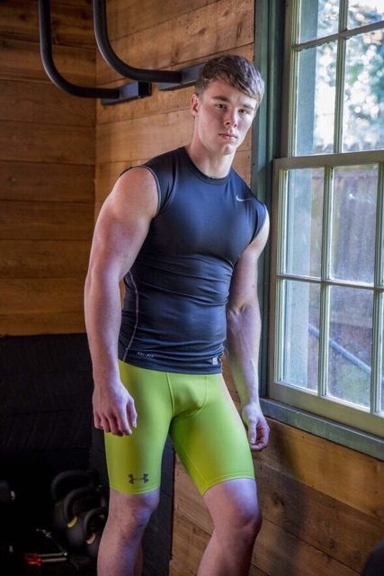 A muscular man in a compression shirt and shorts stands in a gym.