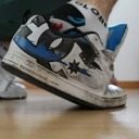 A person wears white and blue sneakers with white patterned socks on a wooden floor.