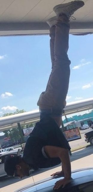 A man performs a handstand on the roof of a car in an outdoor setting.