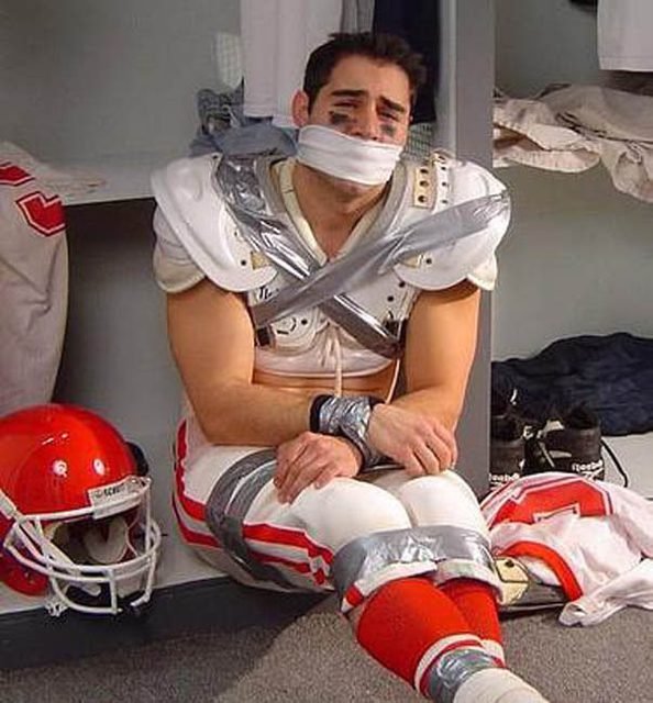 A man in a football uniform is gagged and restrained with tape in a locker room.