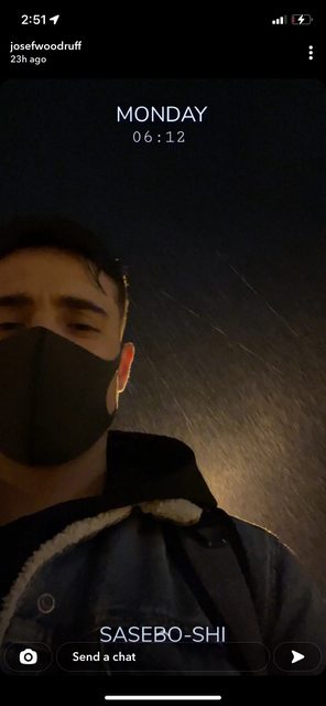 A young man wearing a face mask and a denim jacket stands outdoors at night.