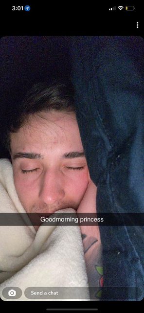 A young man with tattoos sleeps peacefully under a blanket in bed.