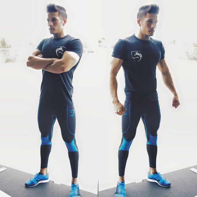 A muscular man poses in dark compression sportswear and blue sneakers.