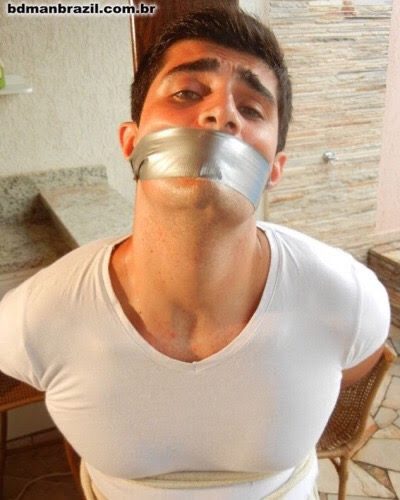 A man is gagged with duct tape and bound with rope in an indoor setting.