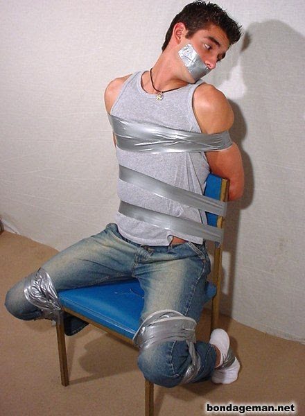 A muscular man is restrained to a blue chair with silver tape, with his mouth also taped.