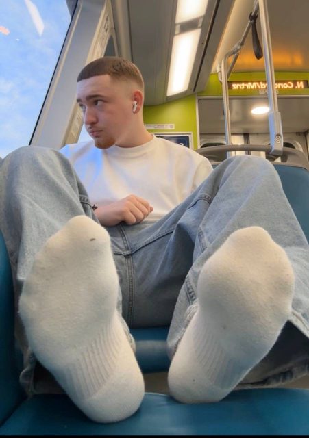A young man rests his socked feet on a seat inside a train.