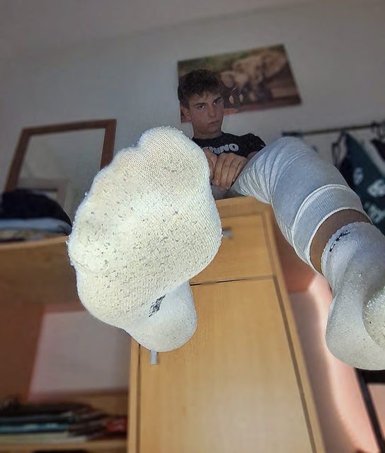 A young man with white socks on his feet is relaxing in a bedroom.