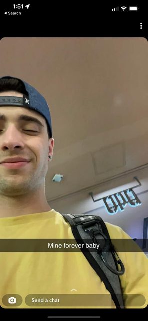 A young man in a cap and yellow t-shirt smiles in an indoor setting.