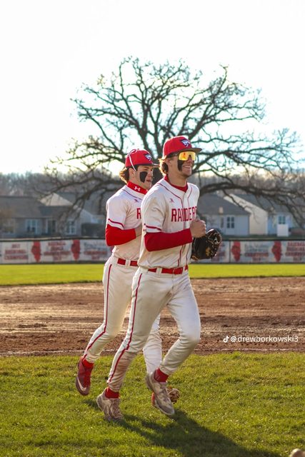 Two baseball players in uniform run across a field.