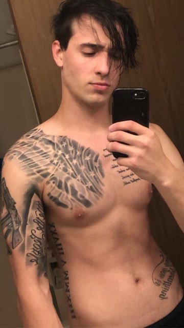 A shirtless man with dark hair and tattoos takes a mirror selfie.