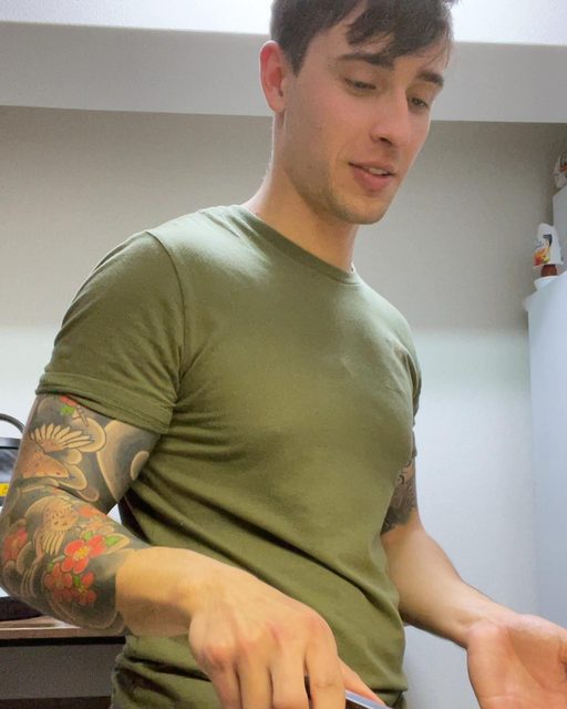 A man with tattoos wearing a green t-shirt is focused on a task indoors.