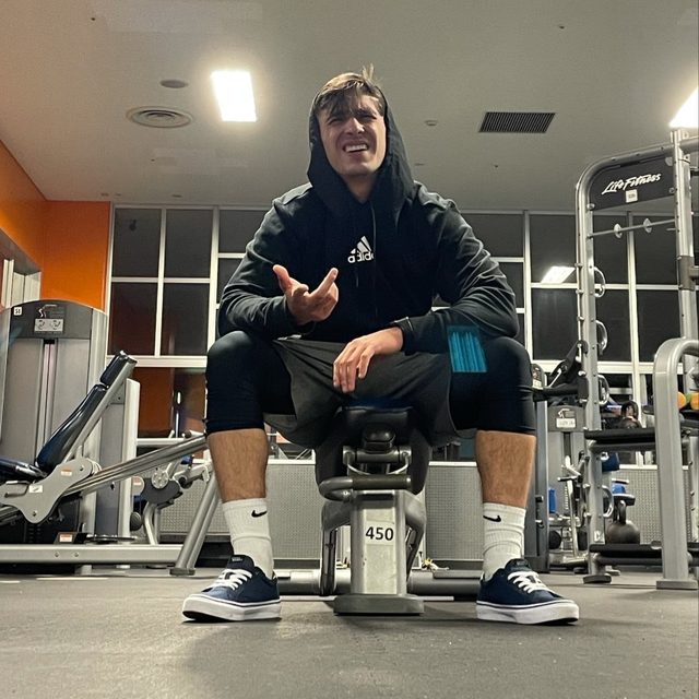 A young man in sportswear sits on a bench in a gym.