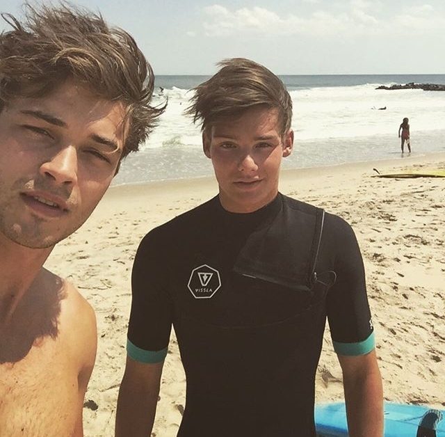 Two young men pose for a selfie on a sunny beach.