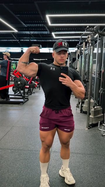 A muscular man in sportswear poses for a selfie in the gym.