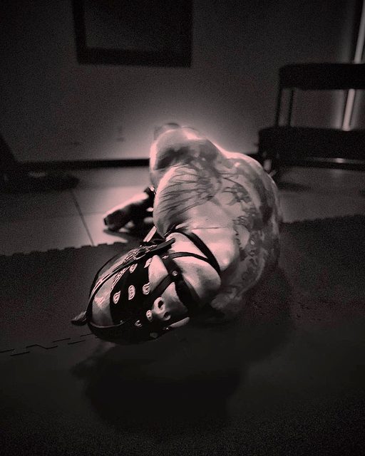 A man in a rubber suit and mask lies on a dark floor.