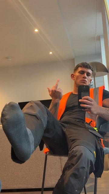 A jock in a work uniform and socks takes a selfie, showing his middle finger.