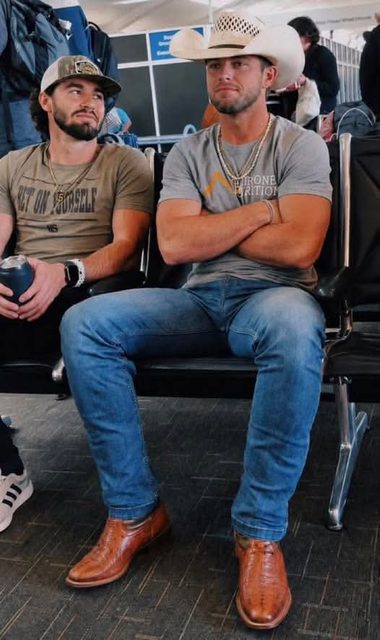 Two men are seated in a public area, one wearing a cowboy hat and boots, and the other wearing a cap.