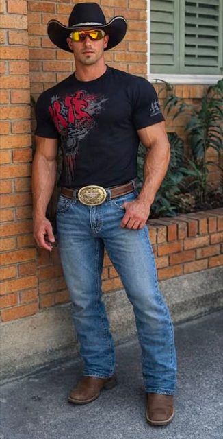 A muscular man in a cowboy hat, sunglasses, t-shirt, and jeans stands outdoors against a brick wall.