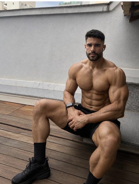 A muscular man in sportswear sits on a wooden deck outdoors.