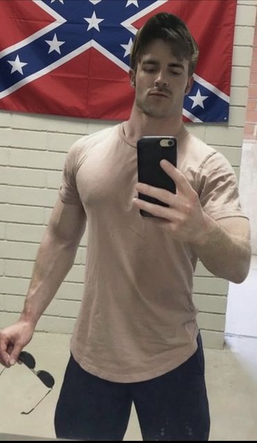 A muscular man takes a mirror selfie while holding sunglasses.