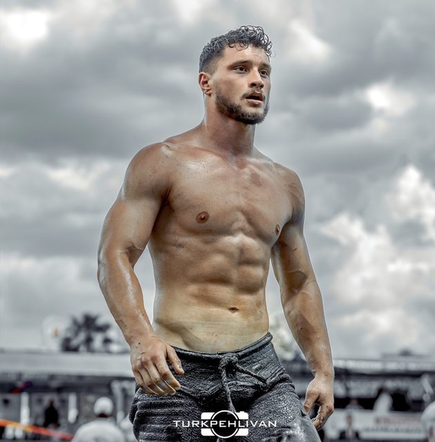 A muscular man wearing traditional wrestling pants stands outdoors under a cloudy sky.