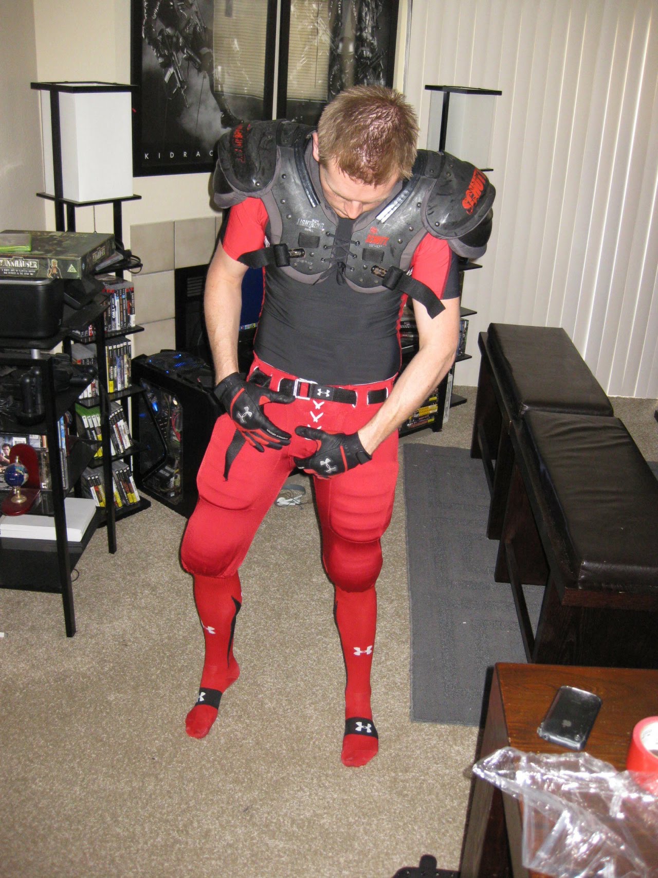 A man stands in a room wearing red and black sports gear, adjusting his pants.