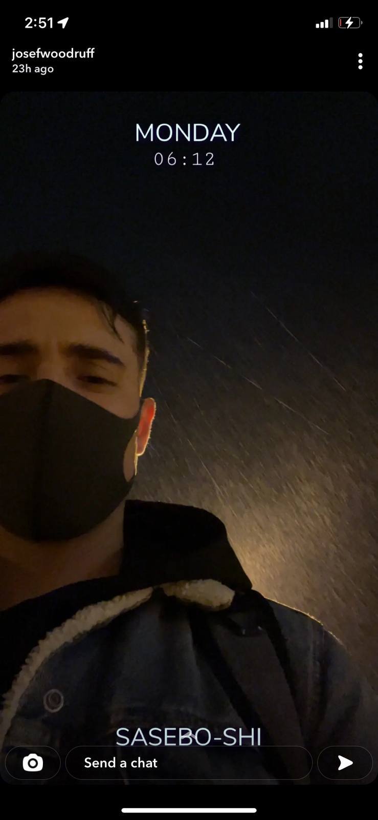 A young man wearing a face mask and a sherpa-lined denim jacket stands outdoors at night in the rain.