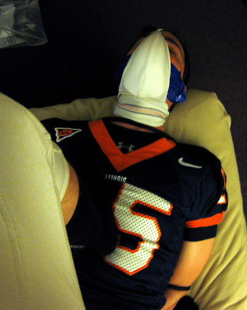A person wearing a sports jersey is blindfolded and restrained on a bed.
