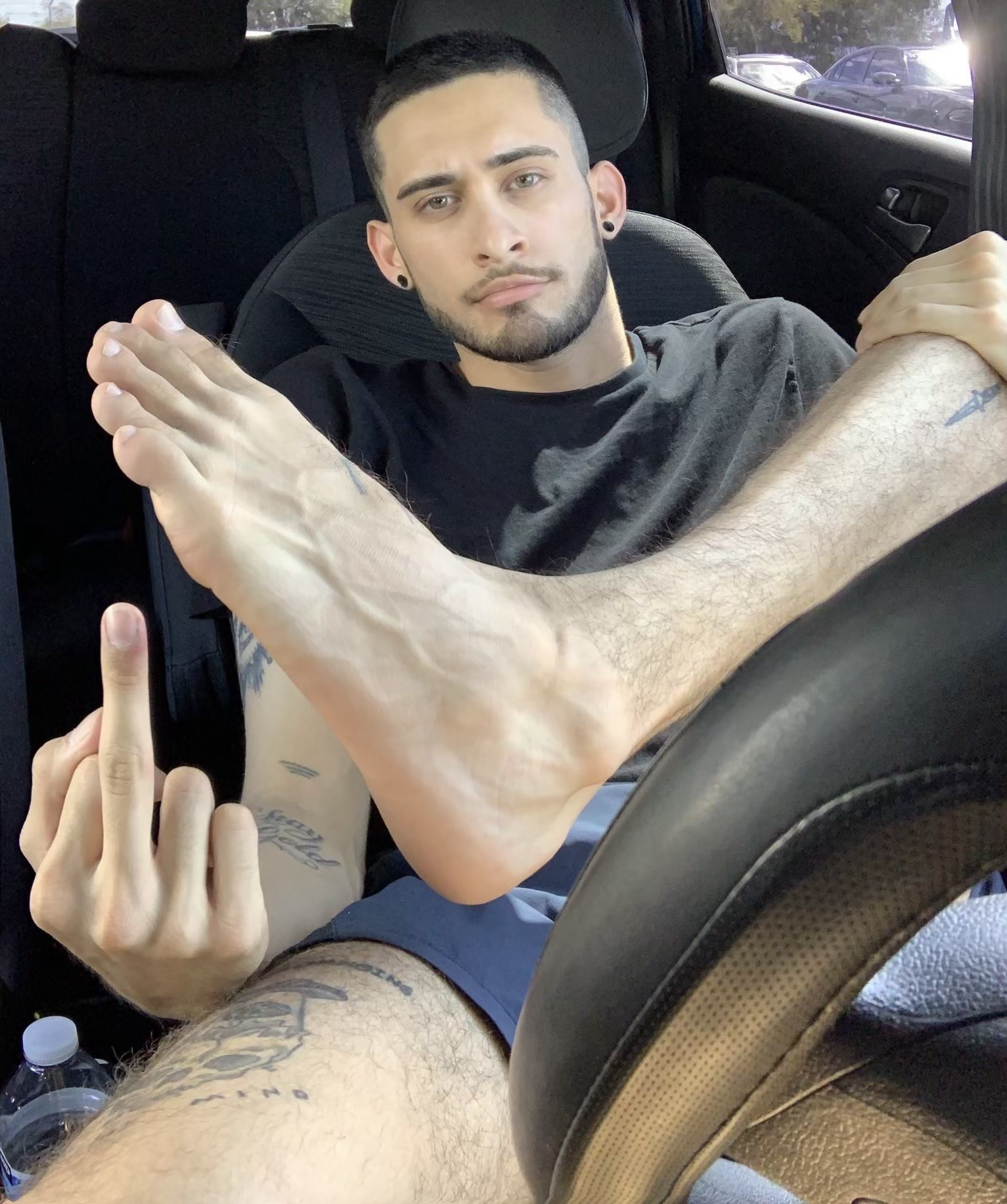 A man in a car holds one bare foot up while giving the middle finger.