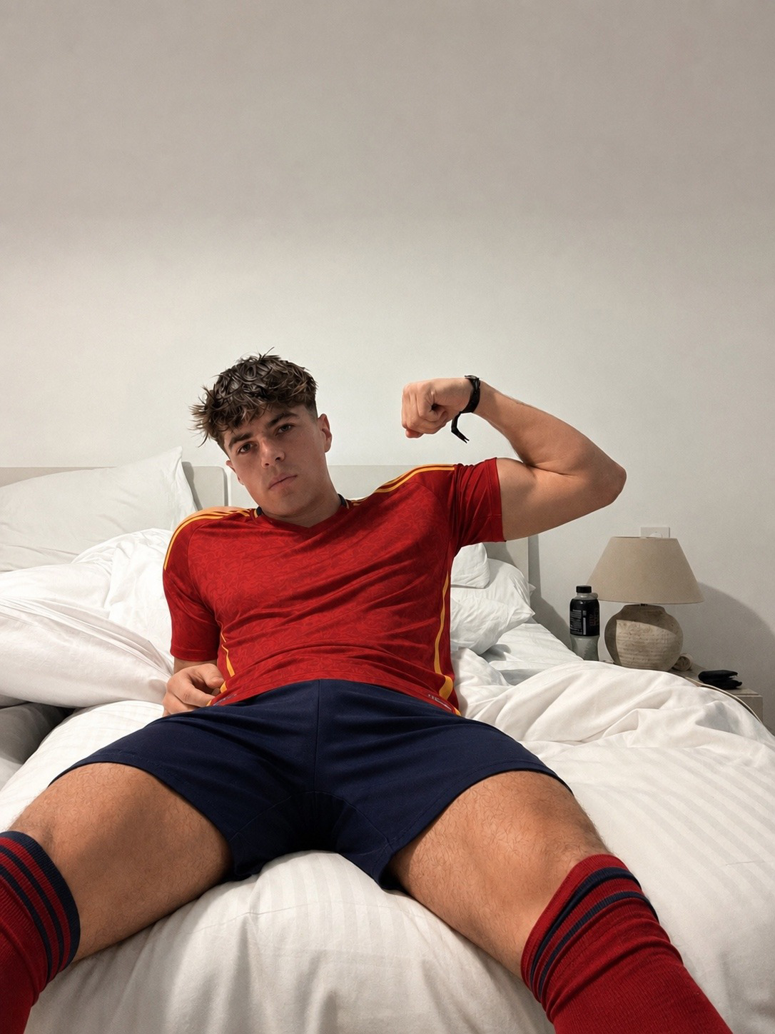 A muscular man in sportswear poses on a bed in a bedroom.