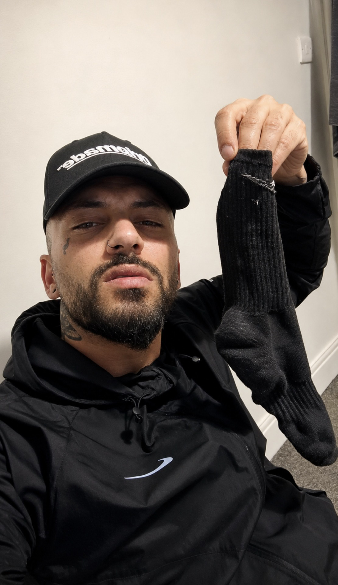 A man in a black cap and hoodie holds up a black sock.